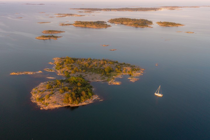 Aerial view of islands with a sailboat on calm water during sunset.