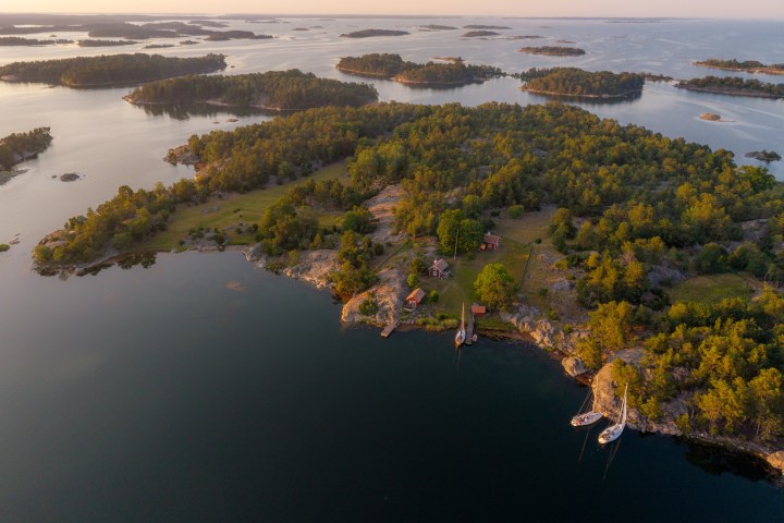 Aerial view of forested islands with houses, surrounded by calm waters at sunset.
