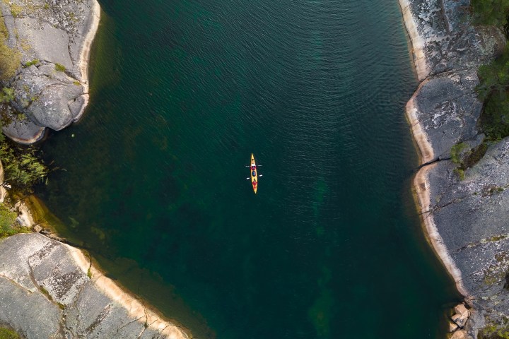 Aerial view of a kayak in a narrow river surrounded by rocky cliffs and trees.