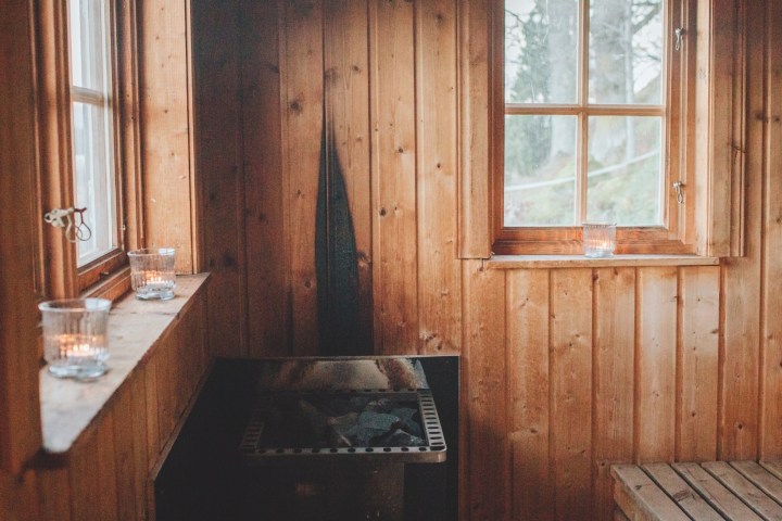 Wooden sauna interior with two windows, a heater, and lit candles on the sill.