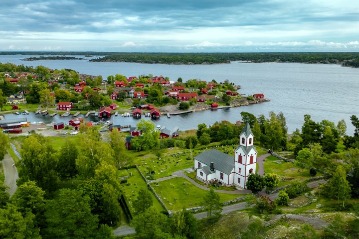 Aerial view of a village by a lake with red houses and a white church surrounded by greenery.