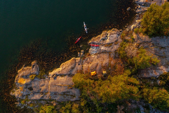 Aerial view of two kayaks, tents, and rocky shoreline with trees.