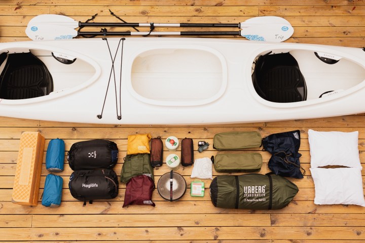 Kayak and camping gear on wooden deck, including paddles, bags, and pillows.