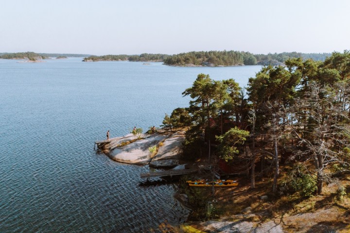 Person on rocky island with trees, surrounded by calm water and distant landmasses.