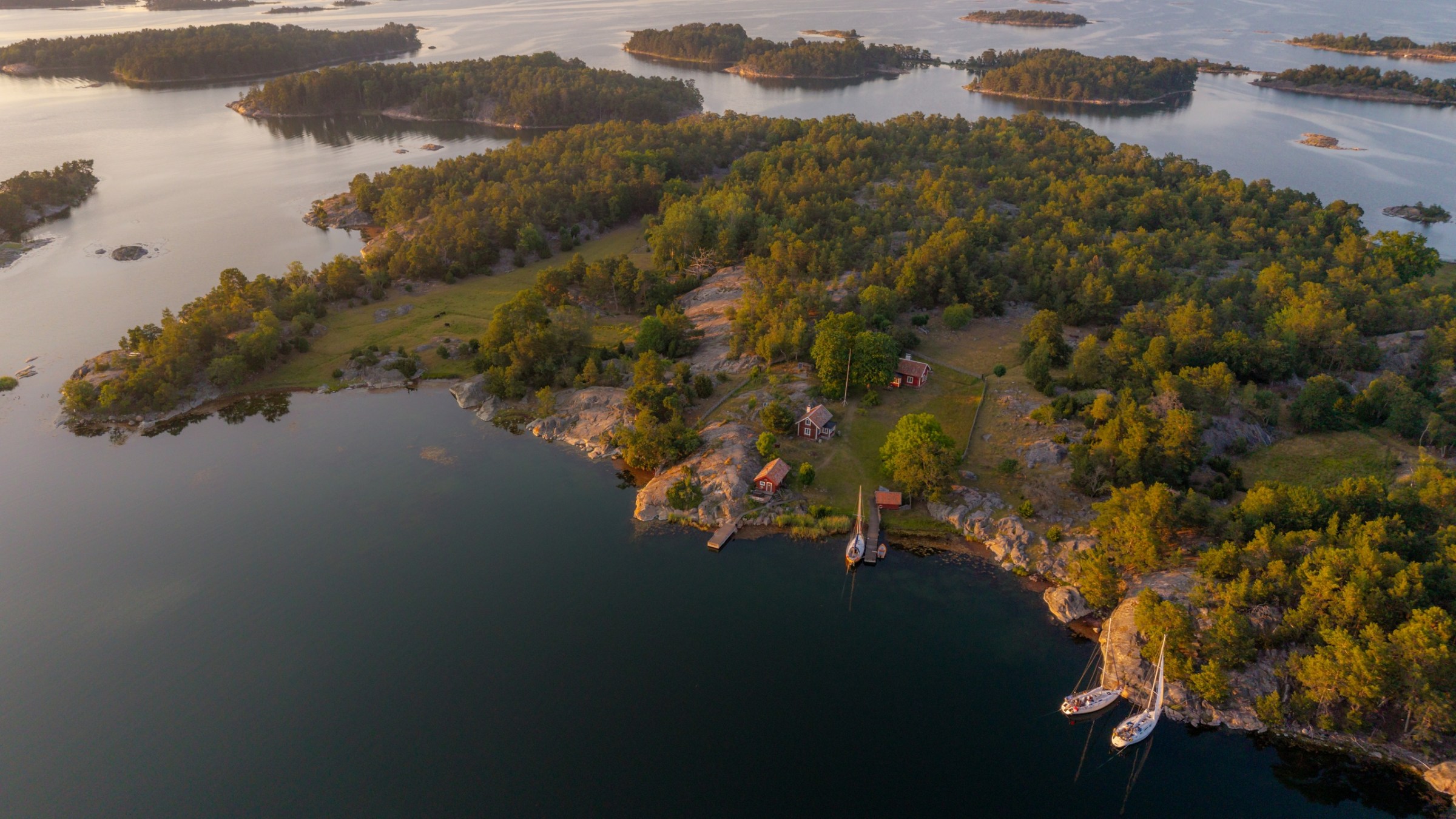 Aerial view of green islands and boats on calm water at sunrise or sunset.