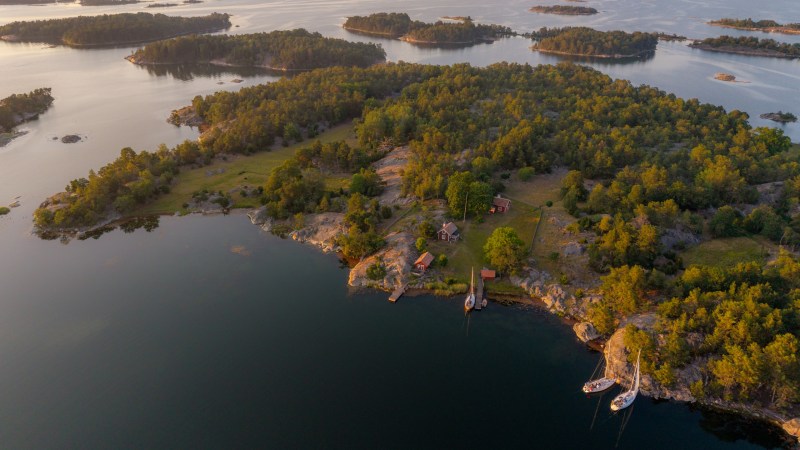 Aerial view of green islands and boats on calm water at sunrise or sunset.