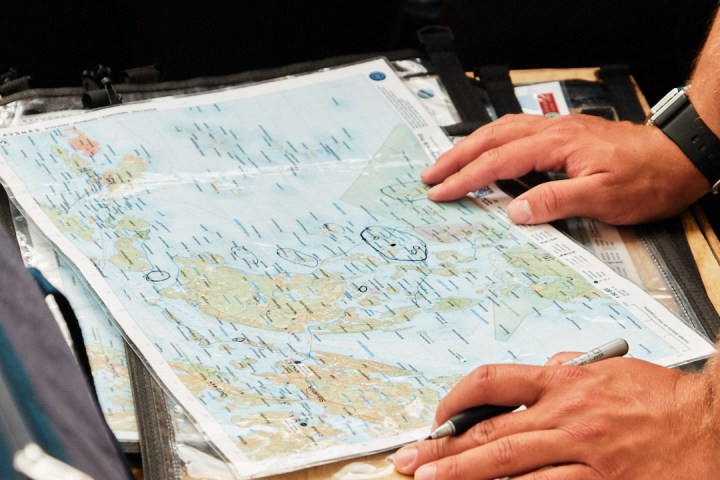 Person with pen marking a map on a table surrounded by bags.