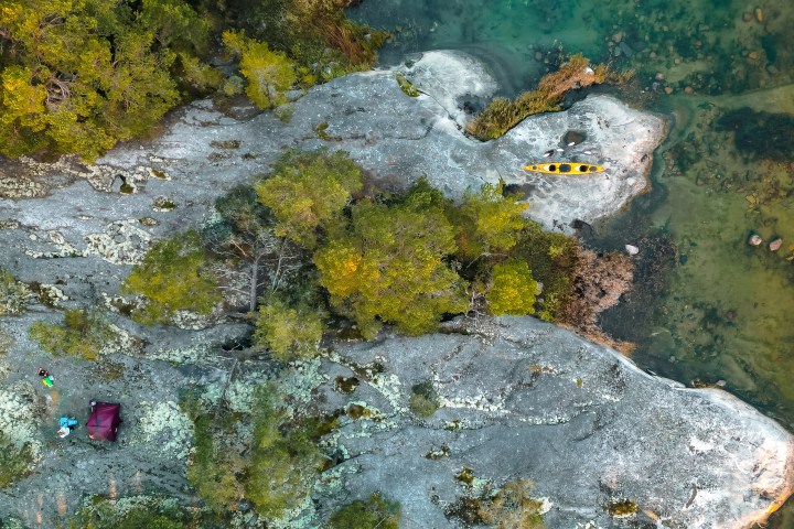 Aerial view of a kayak by rocky shore, surrounded by trees and clear water.