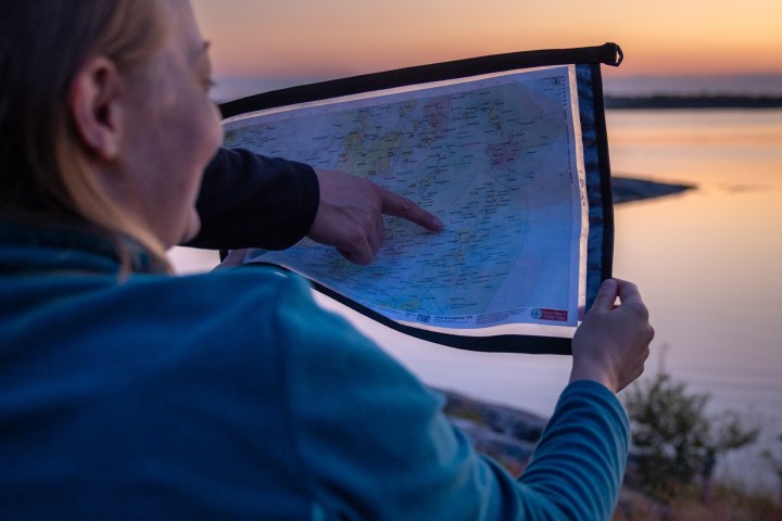 Two people outdoors at sunset, one holding a map, the other pointing at it.