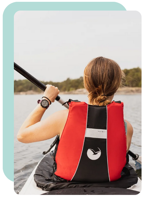 Person in a red life jacket kayaking on calm water, view from behind.