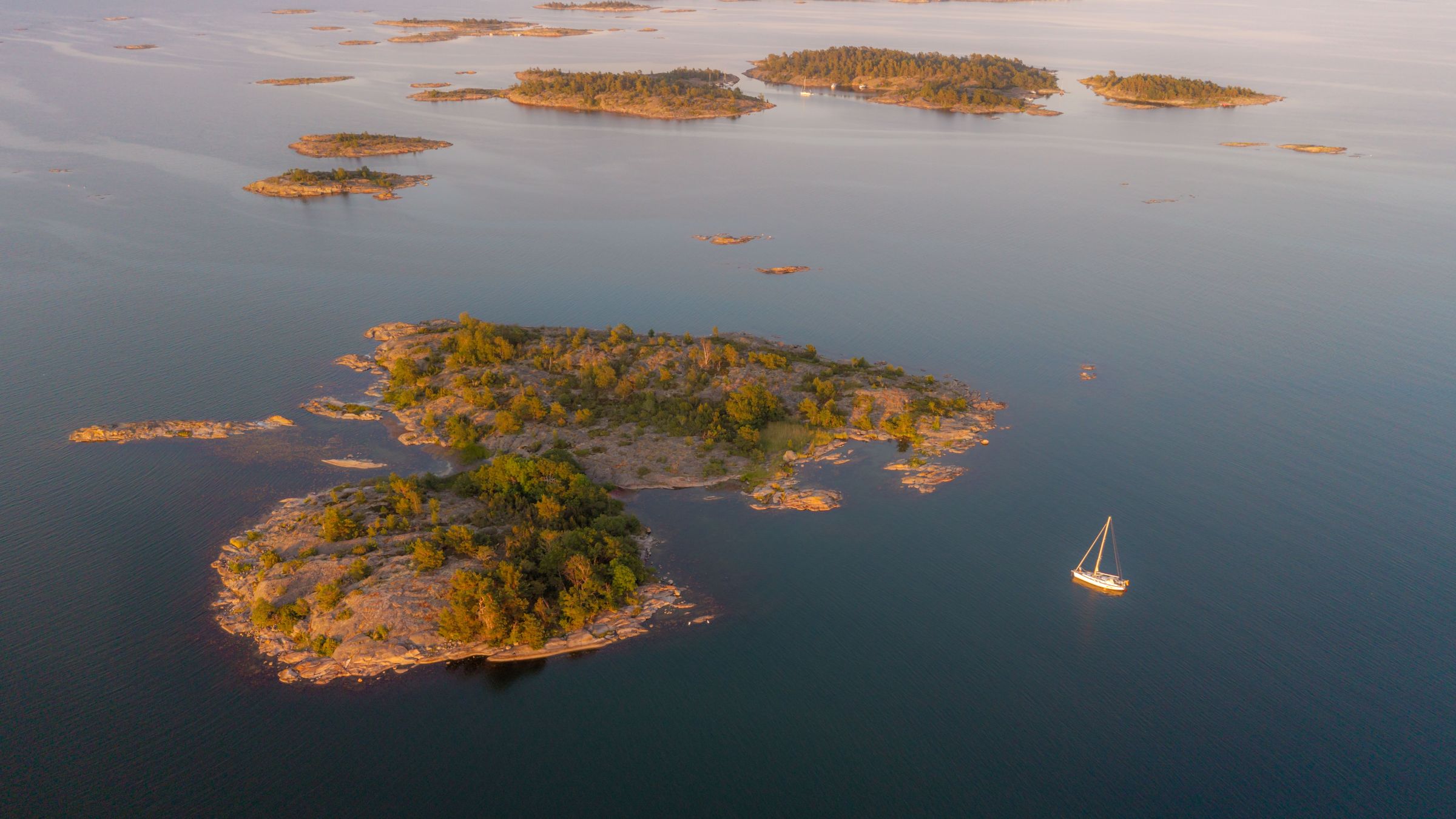 Aerial view of small, tree-covered islands and a sailboat on calm water.