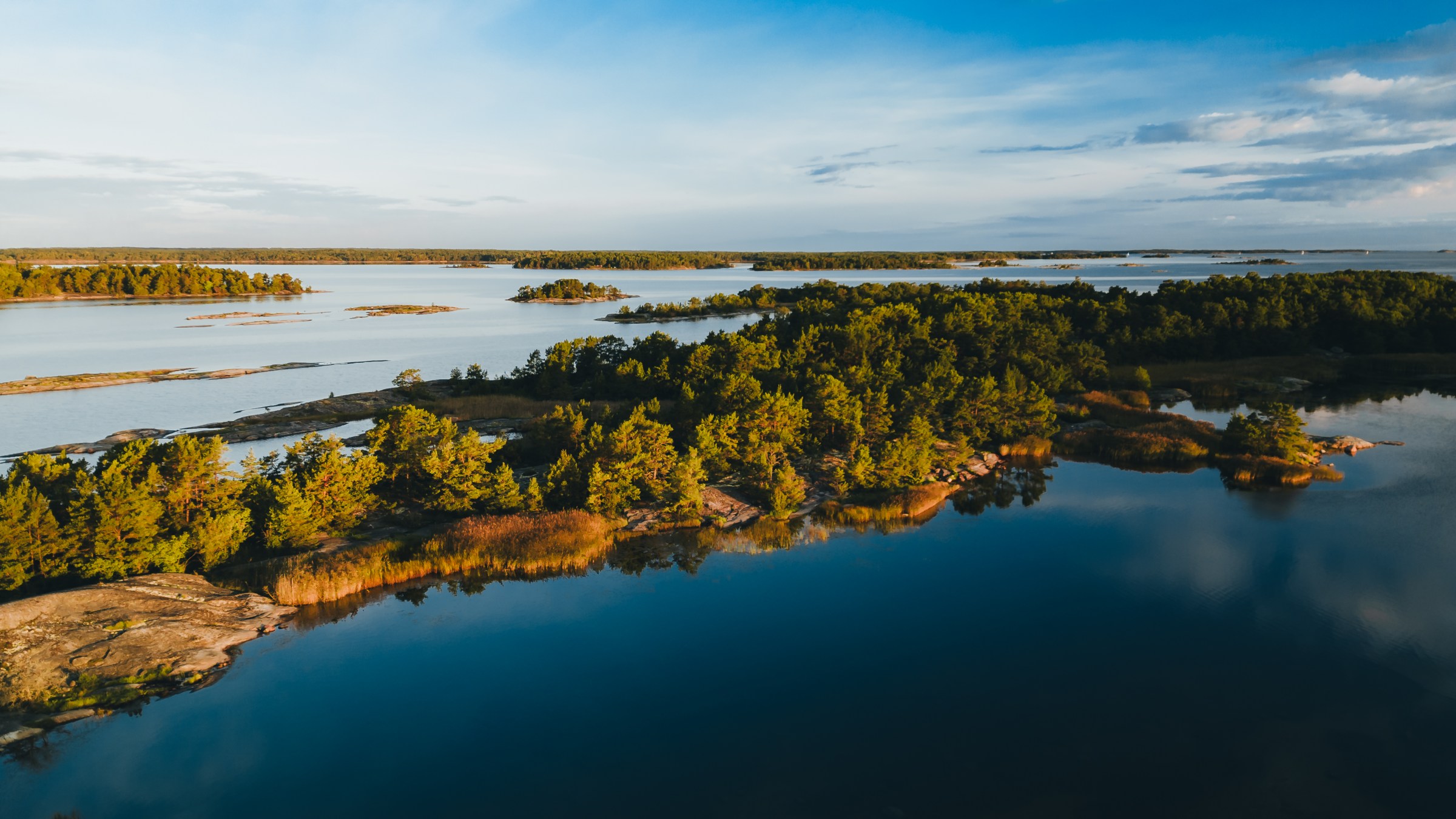 Aerial view of forested islands surrounded by calm blue water under a clear sky.