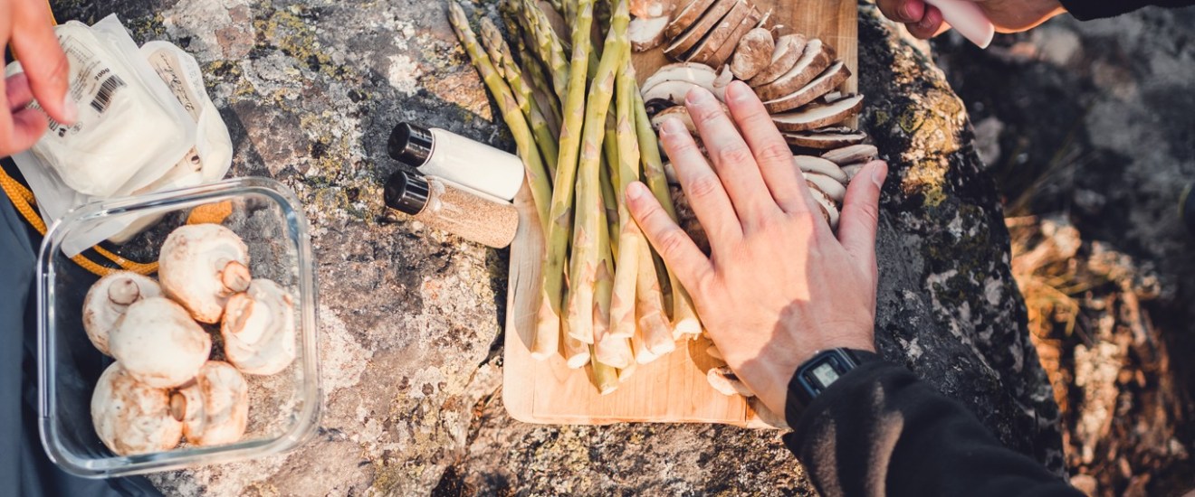 People preparing asparagus and mushrooms on a cutting board outdoors.