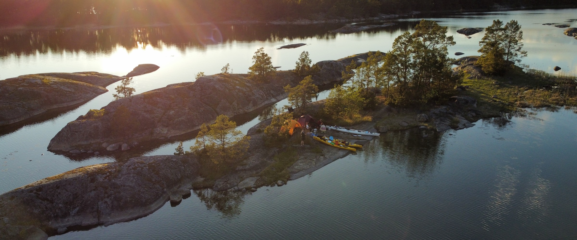 Aerial view of tents on rocky island with trees and surrounding water.