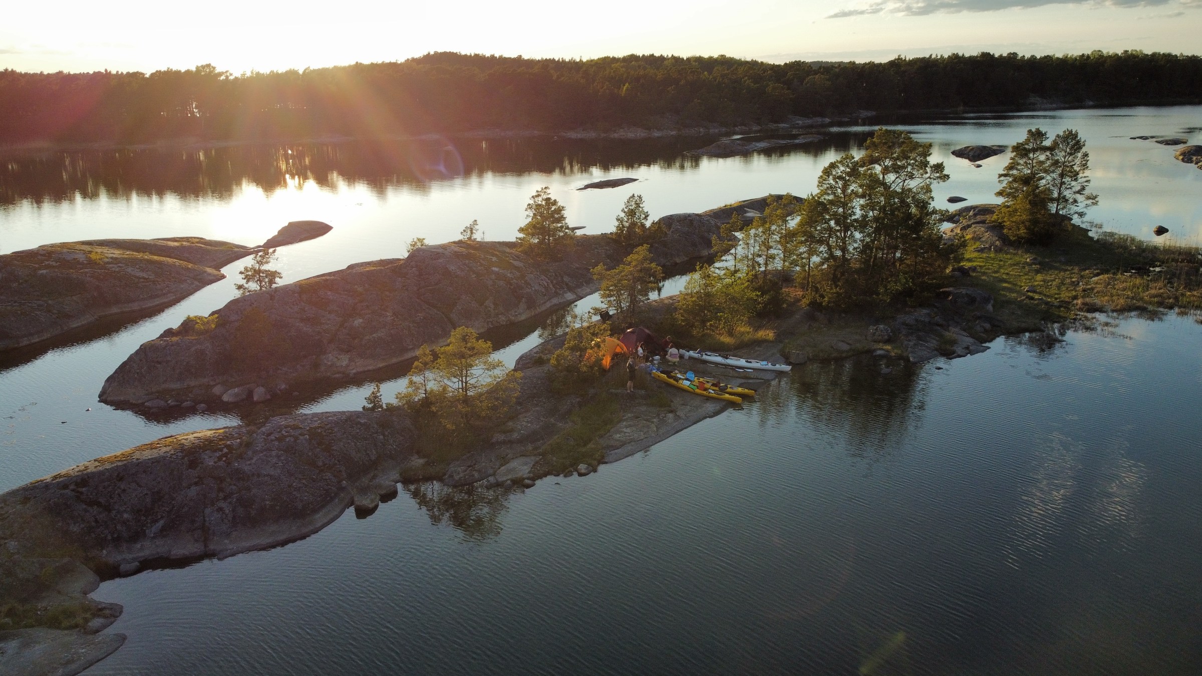Aerial view of tents on rocky island with trees and surrounding water.